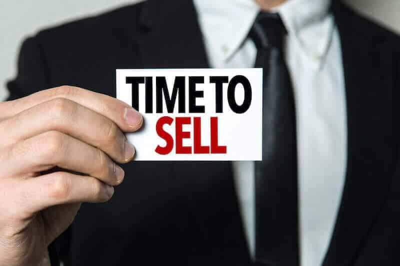 man holding time to sell sign - sell my house now or wait